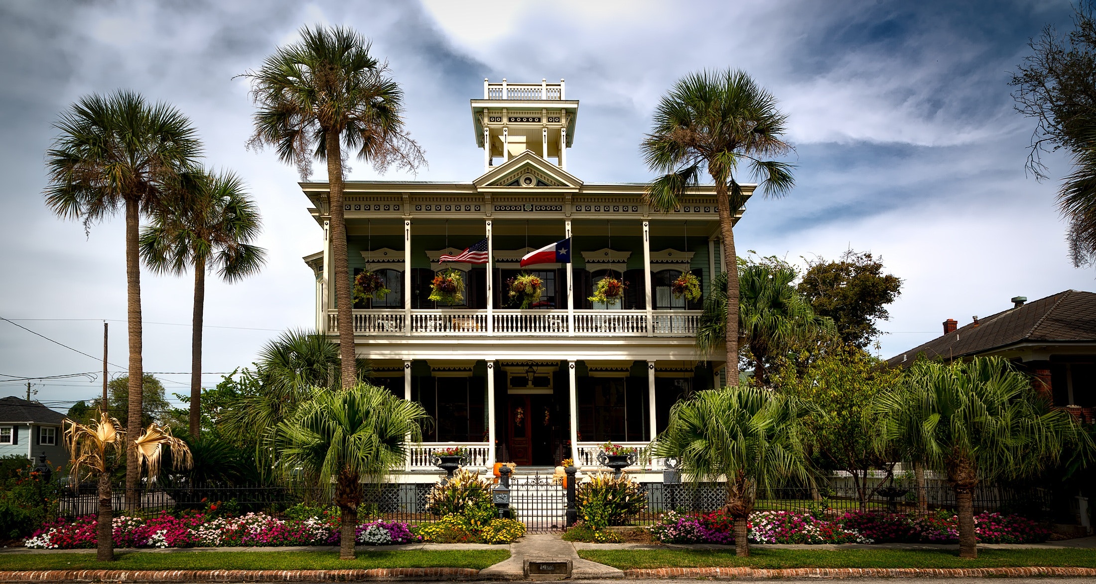 A massive house with a beautiful garden and flowers surrounding it.