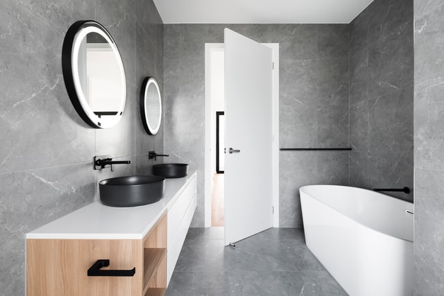 A bathroom with tub, tiles, mirrors, faucets and fixtures.